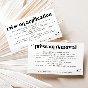 Może przedstawiać: Dwie białe karty z instrukcjami dotyczącymi nakładania i usuwania paznokci typu press-on. Karty mają czarny tekst i gwiazdki. Tło przedstawia suszony liść palmy.