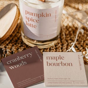 May include: A clear glass candle with a wooden wick, labeled "pumpkin spice latte." Two small cards read "cranberry woods" and "maple bourbon." The candle is 8 oz.