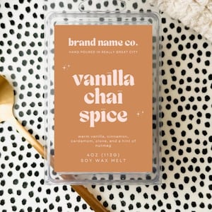 Puede incluir: Un derrite de cera de soja en un recipiente de plástico transparente con el texto "Vanilla Chai Spice" en una etiqueta marrón. La etiqueta también enumera los ingredientes y el nombre de la marca. El derrite está sobre una bandeja de lunares blancos y negros con una cuchara dorada y un palito de madera.