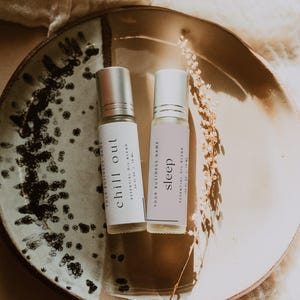 May include: Two clear glass roller bottles with silver caps, each containing an essential oil blend. The left label reads chill out, and the right label reads sleep. Both labels state 0.34 fl oz | 10 ml and Your Business Name.