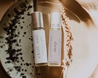 May include: Two clear glass roller bottles with silver caps, each containing an essential oil blend. The left label reads chill out, and the right label reads sleep. Both labels state 0.34 fl oz | 10 ml and Your Business Name.
