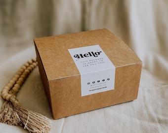 May include: A square brown cardboard box featuring a white rectangular sticker on the top and front. The sticker displays the text Hello, This package is happy to see you too, social media icons, a website placeholder, and brand name here.