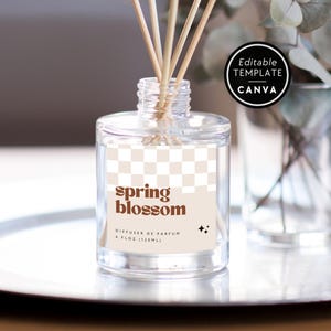 May include: A clear glass reed diffuser bottle with a beige and white checkered label featuring the brown text spring blossom, diffuser de parfum, and 4 fl oz (120ml). Several wooden reeds extend from the top of the bottle.