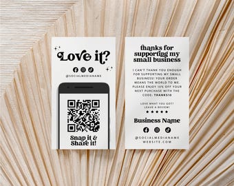 May include: Two white rectangular business cards with black text and graphics. The left card features a smartphone illustration with a QR code, social media icons, and the text Love it? Snap it & Share it!. The right card displays thanks for supporting my small business, a discount code, review request, and contact details.