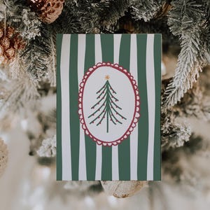 May include: A Christmas card with a green and white striped background. The card features a Christmas tree illustration inside a red scalloped oval. The tree is green with red ornaments and a gold star.