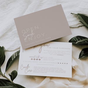 May include: A rectangular taupe card with the text OPEN. Smile ENJOY. awesome business name, layered over a white card with the text Thank you FOR YOUR PURCHASE, connect with us, and Candle Care instructions including trim your wick to 1/4 in.