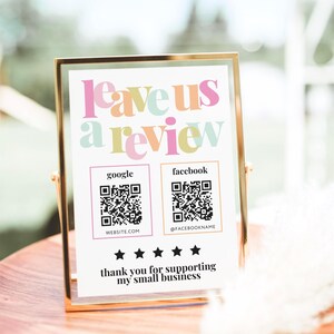 Puede incluir: Un letrero rectangular en un marco de metal dorado con el texto Leave us a review en letras coloridas. Incluye dos códigos QR para Google y Facebook, cinco estrellas negras y el texto thank you for supporting my small business.