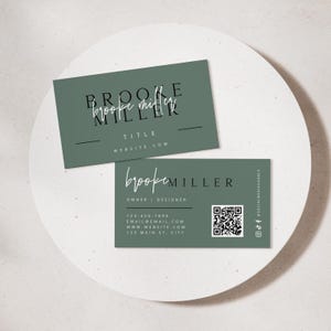 May include: Two business cards with a sage green background. The top card reads "Brooke Miller" in a stylish font, with "Title" and "website.com" below. The bottom card has "Brooke Miller" again, with contact info and a QR code.