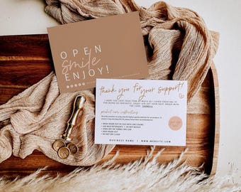 Op de afbeelding: Een bruine kaart met de tekst OPEN SMILE ENJOY en een witte kaart met de tekst thank you for your support en onderhoudsinstructies, vergezeld door een gouden waszegelstempel en drie kleine waszegels op een houten plank.