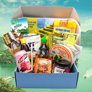 Op de afbeelding: Een blauwe doos gevuld met verschillende ingrediënten voor het maken van Vietnamese loempia's. De doos bevat rijstpapier, rijstnoedels, sojasaus, een blik lychee-sap, een pot uien en een zak gedroogde citroengras. De doos is open en de ingrediënten zijn zichtbaar.