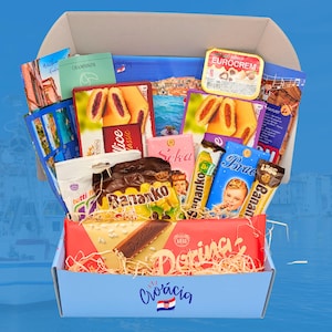 Op de afbeelding: Een blauwe doos met het woord "Croácia" en een Kroatische vlag erop gedrukt. De doos is gevuld met een verscheidenheid aan Kroatische snacks en lekkernijen, waaronder chocolade repen, koekjes en een smeersel. De snacks zijn op een visueel aantrekkelijke manier gerangschikt, met sommige die uit de doos steken.