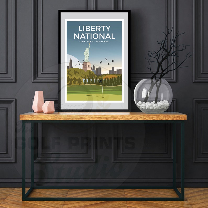 May include: A black framed print of a golf course with the Statue of Liberty in the background. The print has the text "Liberty National" and "13th. Par 5 - 563 Yards."