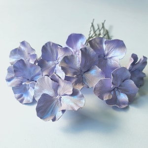May include: A set of lavender fabric flower hair clips. The flowers are arranged in a cluster and have a subtle shimmer.