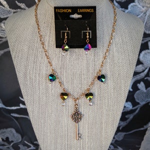 May include: A gold necklace with a key pendant and iridescent heart charms. Matching iridescent heart earrings are included. The necklace and earrings are displayed on a mannequin.