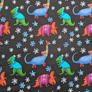 May include: A repeating pattern on a black background features colorful dinosaurs wearing winter hats and sweaters, interspersed with snowflakes. The dinosaurs are in shades of blue, green, purple, and orange, creating a whimsical, festive design.