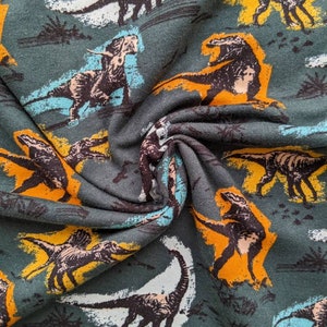 May include: Green fabric with a repeating pattern of dinosaurs in various colors, including orange, yellow, white, and black.
