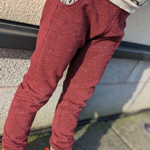 K&ouml;nnte beinhalten: Rote Jogginghose mit gesprenkelter Textur und einer kleinen Tasche vorne. Die Jogginghose wird von einer Person mit bunten Socken und Schuhen getragen.