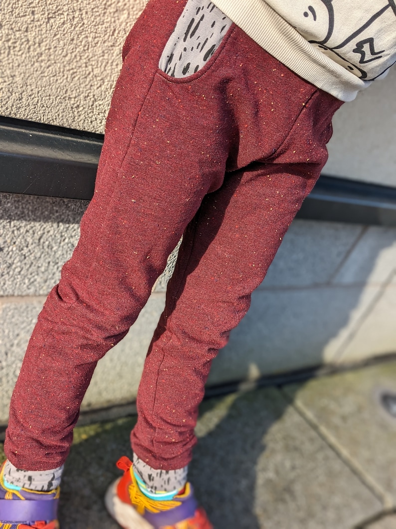 K&ouml;nnte beinhalten: Rote Jogginghose mit gesprenkelter Textur und einer kleinen Tasche vorne. Die Jogginghose wird von einer Person mit bunten Socken und Schuhen getragen.