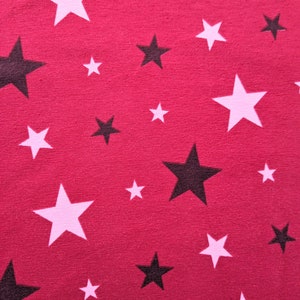 May include: Close-up of a red fabric with a pattern of white and black stars of varying sizes. The stars are scattered across the surface, creating a playful and dynamic design. The fabric has a soft, textured appearance.