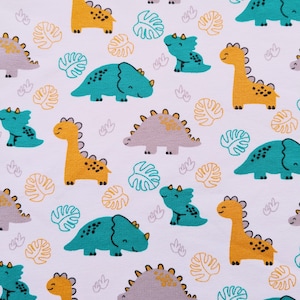 May include: White fabric with a repeating pattern of cartoon dinosaurs in yellow, teal, and gray. The dinosaurs are interspersed with yellow and teal leaf shapes. The design is suitable for children's apparel or nursery decor.