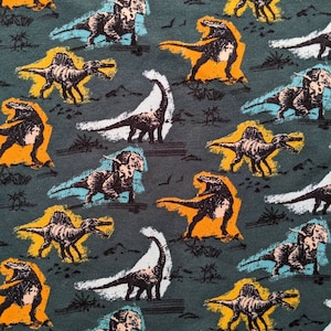May include: A green fabric with a repeating pattern of dinosaurs in various colors, including orange, yellow, white, and blue. The dinosaurs are stylized and have a cartoonish appearance.