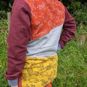 K&ouml;nnte beinhalten: Ein lang&auml;rmliges Shirt in Rot, Grau und Gelb mit einem Tiermuster auf R&uuml;cken und Unterseite. Das Shirt hat einen Rundhalsausschnitt und lange &Auml;rmel.