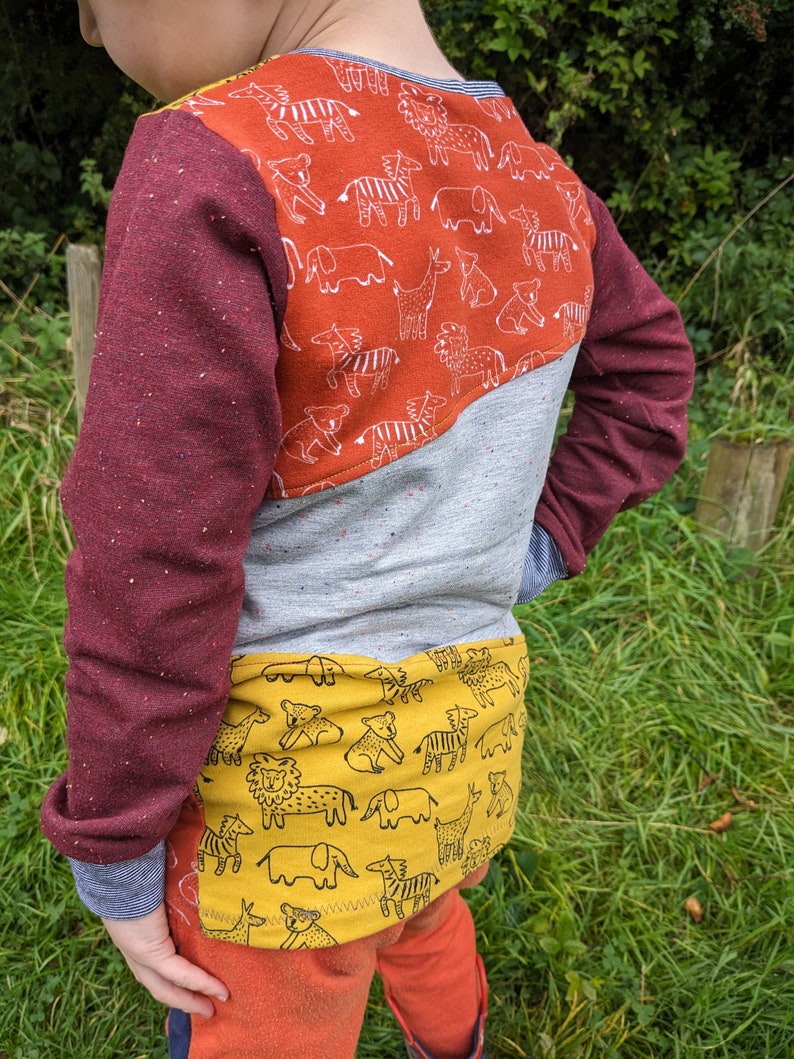 K&ouml;nnte beinhalten: Ein lang&auml;rmliges Shirt in Rot, Grau und Gelb mit einem Tiermuster auf R&uuml;cken und Unterseite. Das Shirt hat einen Rundhalsausschnitt und lange &Auml;rmel.