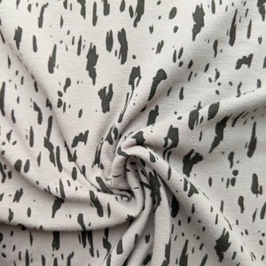 K&ouml;nnte beinhalten: Nahaufnahme eines hellrosa Stoffes mit einem schwarzen abstrakten Druck. Der Stoff ist texturiert und hat ein weiches, flie&szlig;endes Gef&uuml;hl.