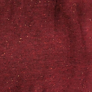 K&ouml;nnte beinhalten: Nahaufnahme eines tief roten Stoffes mit gesprenkelter Textur. Der Stoff hat einen dezenten Glanz und ist mit kleinen Flocken in Gelb, Orange und Blau gewebt.