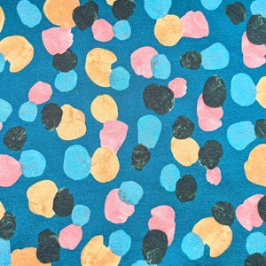 May include: Teal fabric with a repeating pattern of abstract shapes in orange, pink, blue, and black. The shapes vary in size and are scattered across the surface, creating a playful and modern design.