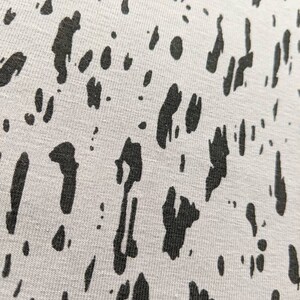 K&ouml;nnte beinhalten: Nahaufnahme eines wei&szlig;en Stoffes mit einem schwarzen abstrakten Muster. Das Muster besteht aus unregelm&auml;&szlig;igen Formen und Linien.