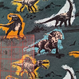 May include: A teal fabric with a repeating pattern of dinosaurs in various colors, including black, white, yellow, and blue. The dinosaurs are outlined in black and have a cartoon-like appearance.