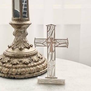 May include: A silver filigree cross with a smaller cross in the centre. The cross is on a silver stand with intricate designs.