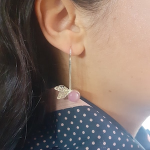 Könnte beinhalten: Ein Paar silberne Ohrhänger mit einem rosa Stein und einem filigranen Schmetterlingsdesign.