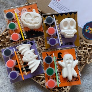 May include: Halloween-themed paint kits with a pumpkin, skull, bat, and ghost. Each kit contains a paintable figure, paint pots, a paintbrush, and embellishments. The kits are packaged in cellophane bags and presented in a cardboard box.