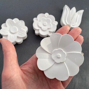 May include: Four white plaster flower shapes, including a tulip, a daisy, and two different styles of flowers with five petals.