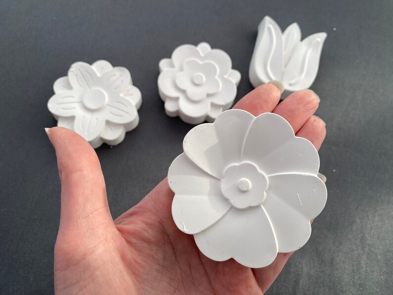 May include: Four white plaster flower shapes, including a tulip, a daisy, and two different styles of flowers with five petals.