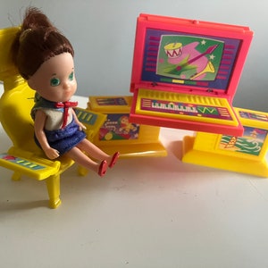 May include: A yellow plastic chair with a doll sitting on it. The doll has brown hair, a blue dress, and red shoes. The chair has a yellow and red keyboard on the armrest. There is a yellow and red computer with a screen showing a musical note and a drum.