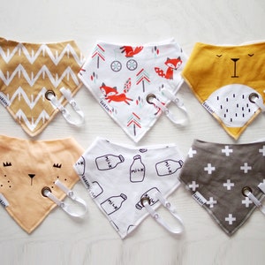 Op de afbeelding: Zes verschillende baby-slabbetjes met verschillende patronen. De slabbetjes zijn gemaakt van zacht katoen en hebben een drukknoop sluiting. De patronen omvatten een chevron-patroon, een vos-patroon, een melkfles-patroon, een plusteken-patroon, een beren-patroon en een geel patroon met een berenkop.