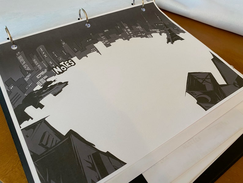 May include: A black and white illustration of a city skyline with the word "Notes" written in white on a black background. The image is printed on a white sheet of paper in a binder.