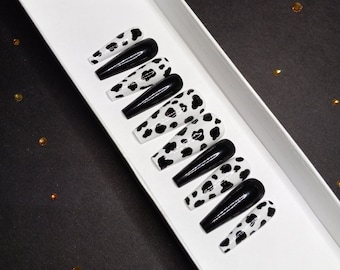 May include: A set of ten long, black and white cow print press-on nails with a black glossy finish.