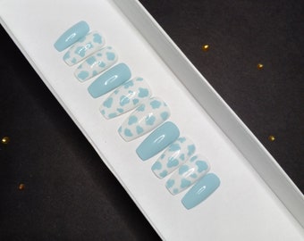 May include: A set of ten blue and white cow print press-on nails in a white box.