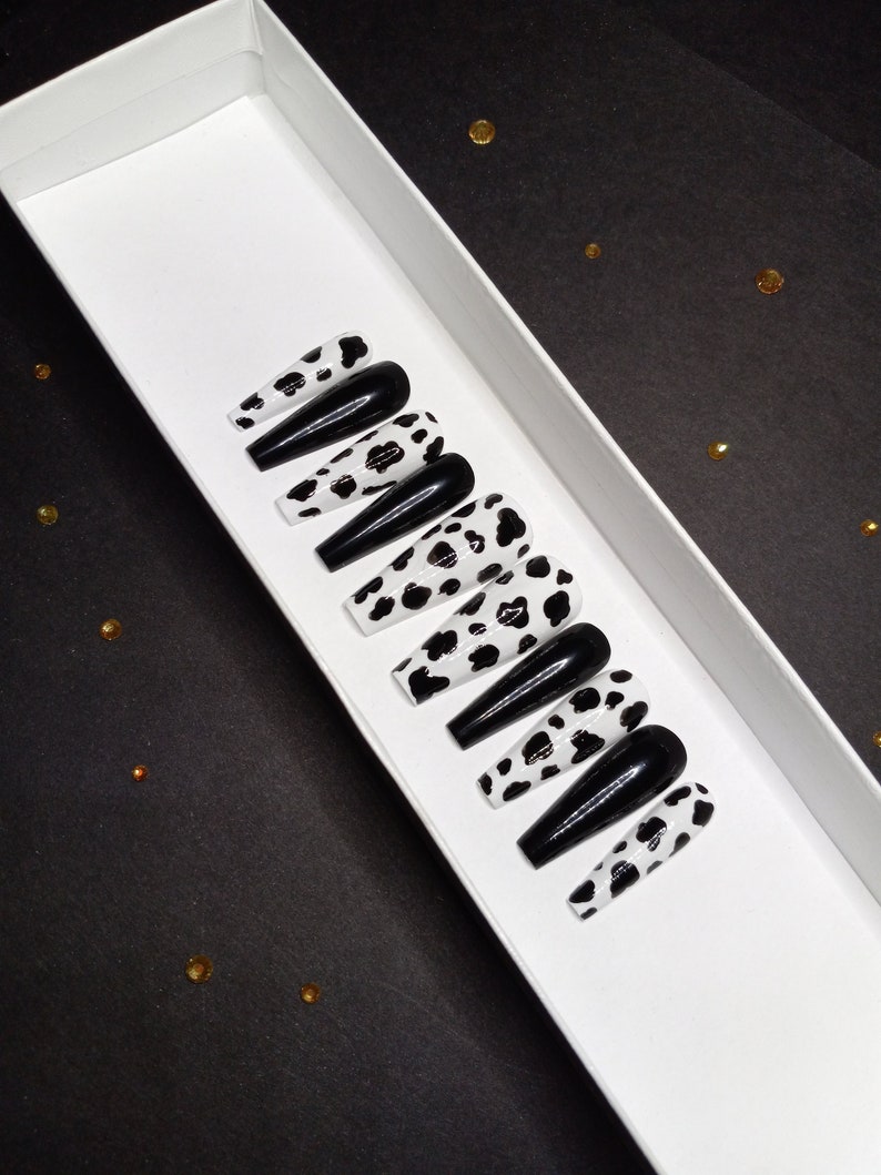 May include: A set of ten long, black and white cow print press-on nails with a black glossy finish.