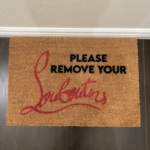May include: A brown coir doormat with the text "PLEASE REMOVE YOUR" in black lettering and a red "Louboutin" logo.