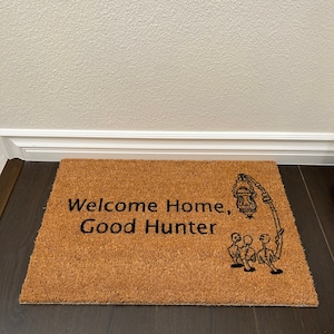 May include: A brown coir doormat with the text "Welcome Home, Good Hunter" and a black and white illustration of three figures holding a lantern.