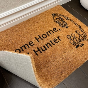 May include: A brown coir doormat with the text "Welcome Home Hunter" and a black silhouette of a lantern and three people.