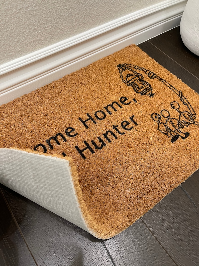 May include: A brown coir doormat with the text "Welcome Home Hunter" and a black silhouette of a lantern and three people.