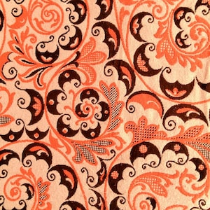 May include: Close-up of a fabric with a repeating floral pattern. The design features swirling vines and stylized flowers in shades of orange and dark brown against a cream background. The pattern is detailed and intricate.