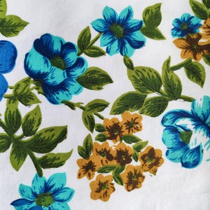 May include: White fabric with a floral pattern featuring blue, teal, and gold flowers with green leaves. The flowers are in various sizes and arrangements, creating a vintage or retro aesthetic.