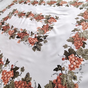May include: White tablecloth featuring a repeating pattern of orange grapes, green leaves, and brown vines. The grape design borders the edges and forms a rectangular frame in the centre. The fabric has a slight sheen.